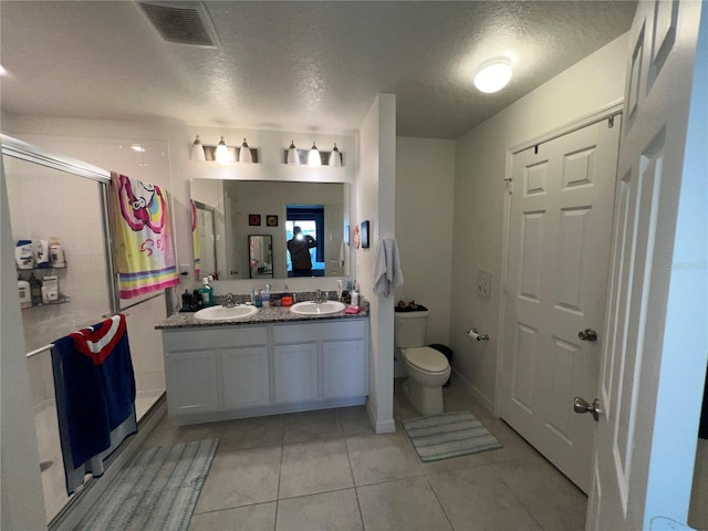 bathroom featuring toilet, a textured ceiling, vanity, a shower with door, and tile patterned flooring