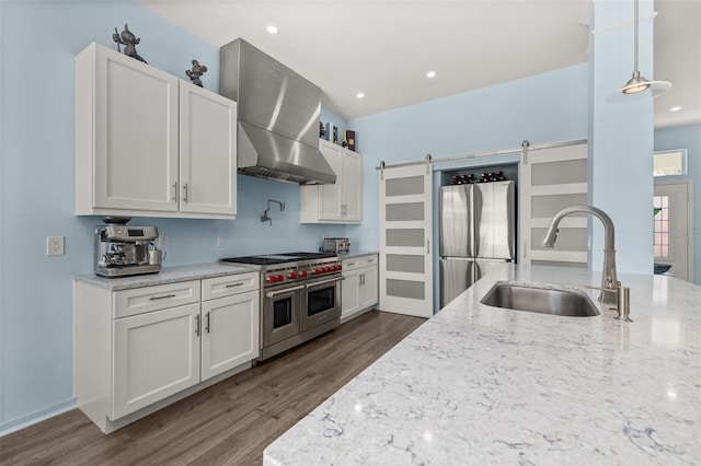 kitchen featuring stainless steel appliances, a barn door, white cabinets, and wall chimney exhaust hood