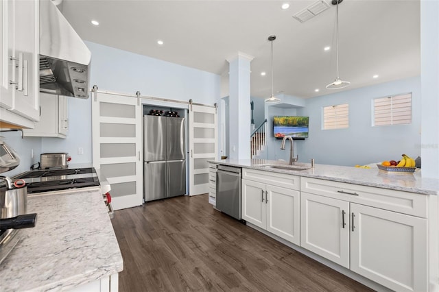 kitchen with appliances with stainless steel finishes, white cabinetry, hanging light fixtures, extractor fan, and a barn door