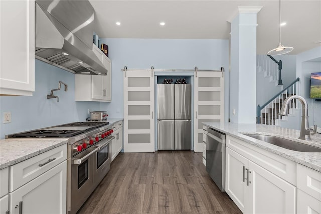 kitchen featuring appliances with stainless steel finishes, white cabinetry, sink, exhaust hood, and a barn door