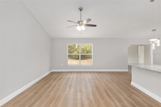 unfurnished living room with ceiling fan with notable chandelier, light hardwood / wood-style flooring, and vaulted ceiling