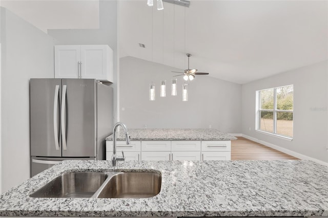 kitchen featuring light stone counters, sink, stainless steel fridge, and white cabinets