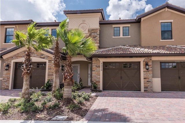 view of front of property featuring a tile roof, decorative driveway, stone siding, and stucco siding