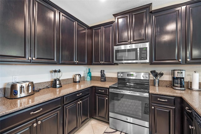 kitchen featuring light tile patterned flooring, appliances with stainless steel finishes, light stone counters, and dark brown cabinetry