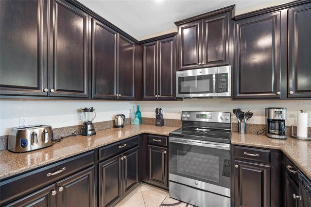 kitchen with light stone countertops, dark brown cabinetry, light tile patterned floors, and stainless steel appliances