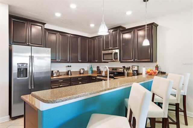 kitchen with a peninsula, stainless steel appliances, dark brown cabinets, decorative light fixtures, and a breakfast bar area