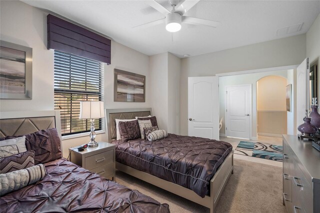 carpeted bedroom with a ceiling fan, arched walkways, and visible vents