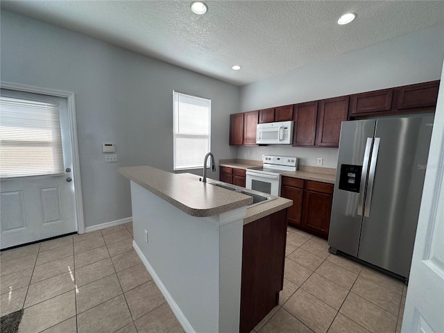 kitchen with a kitchen island with sink, sink, white appliances, and light tile patterned floors