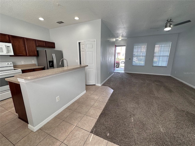 kitchen with dark brown cabinetry, light colored carpet, a center island with sink, a textured ceiling, and white appliances