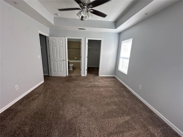 unfurnished bedroom with dark carpet, a raised ceiling, and a textured ceiling