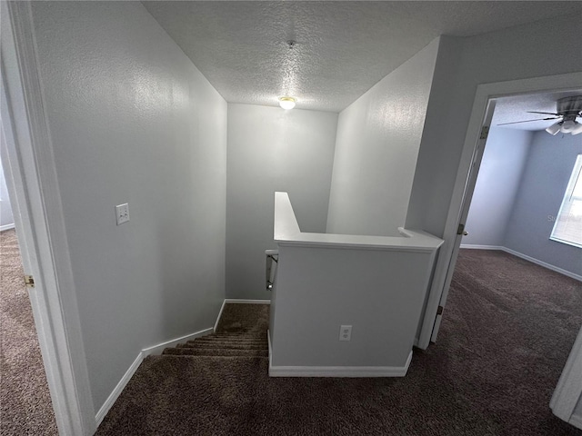 corridor with a textured ceiling and dark colored carpet