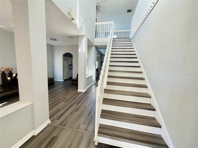 staircase featuring arched walkways, visible vents, baseboards, and wood finished floors