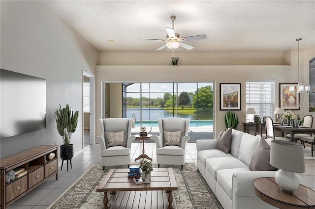 living room with a water view, ceiling fan, a textured ceiling, and light tile patterned floors