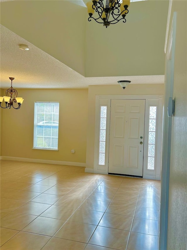 foyer entrance with light tile patterned floors, a textured ceiling, a chandelier, and a towering ceiling