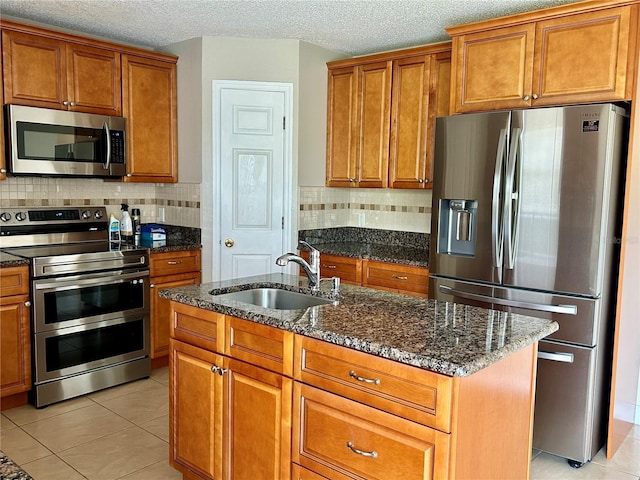 kitchen featuring sink, light tile patterned floors, dark stone counters, an island with sink, and stainless steel appliances