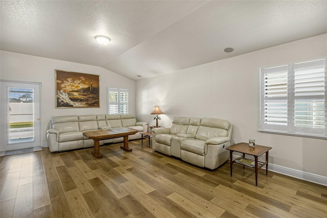 living room with vaulted ceiling, a textured ceiling, and light wood-type flooring