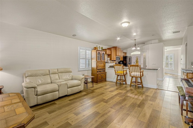 living room featuring a chandelier, vaulted ceiling, a textured ceiling, and light wood-type flooring