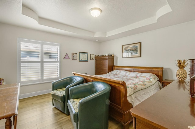 bedroom featuring a raised ceiling, a textured ceiling, and light wood-type flooring