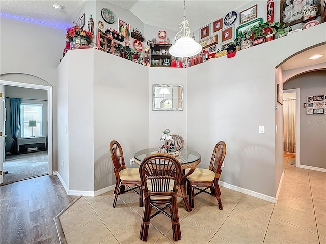 dining space with lofted ceiling, a textured ceiling, and light tile patterned floors