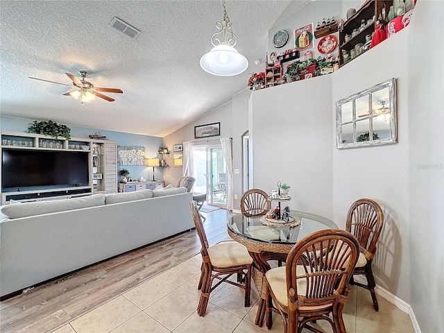 tiled dining space featuring ceiling fan, lofted ceiling, and a textured ceiling