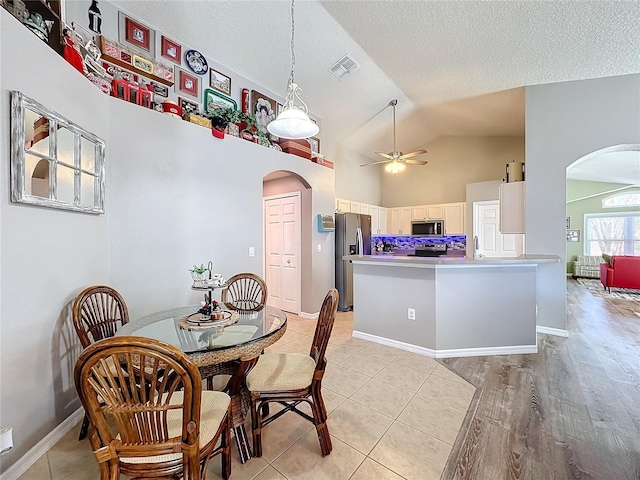 tiled dining area featuring ceiling fan, high vaulted ceiling, sink, and a textured ceiling