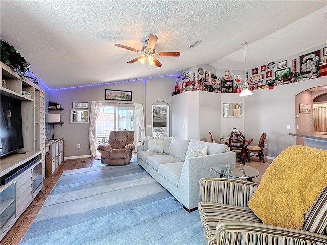 living room with hardwood / wood-style flooring, ceiling fan, lofted ceiling, and a textured ceiling