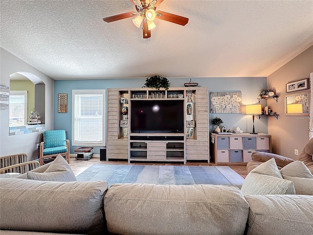 living room featuring ceiling fan, vaulted ceiling, and a textured ceiling