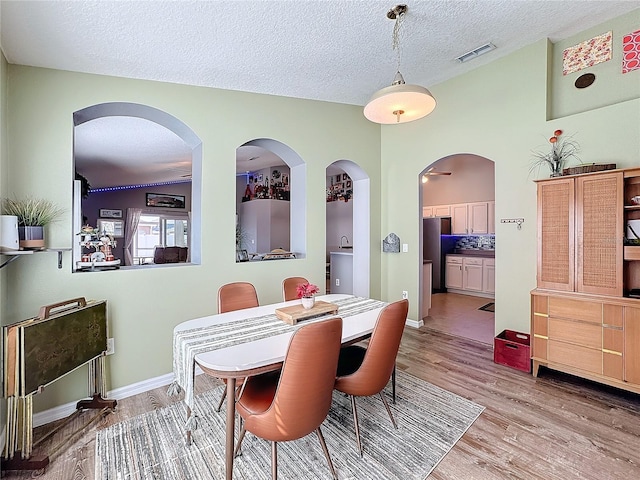 dining area with light wood-type flooring, visible vents, a textured ceiling, and baseboards