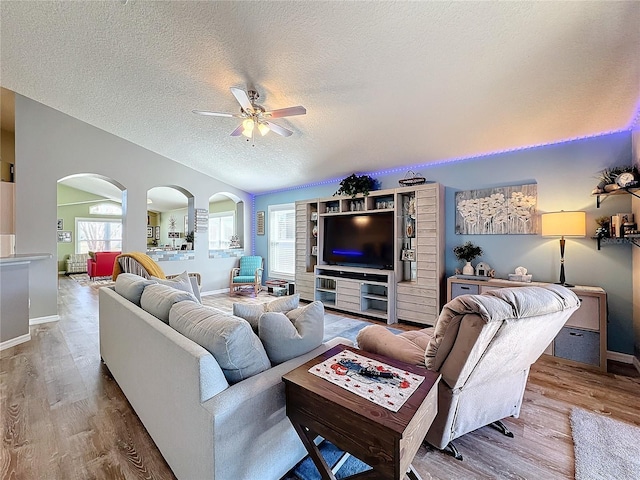 living room featuring lofted ceiling, arched walkways, a textured ceiling, wood finished floors, and a ceiling fan