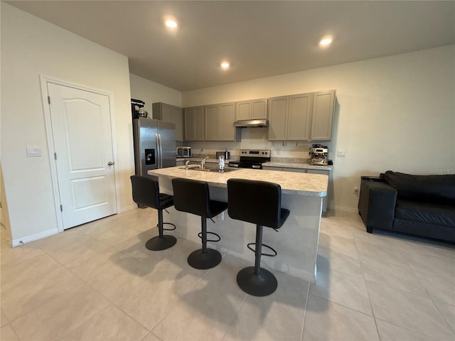 kitchen with gray cabinets, appliances with stainless steel finishes, a kitchen breakfast bar, light tile patterned floors, and a center island with sink