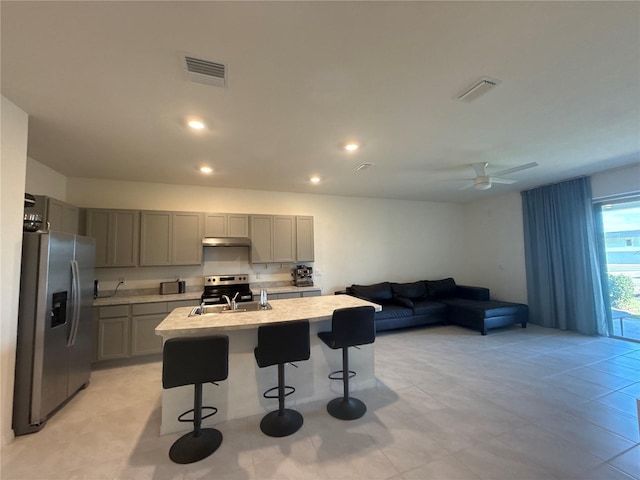 kitchen featuring appliances with stainless steel finishes, sink, gray cabinetry, a kitchen bar, and a center island with sink