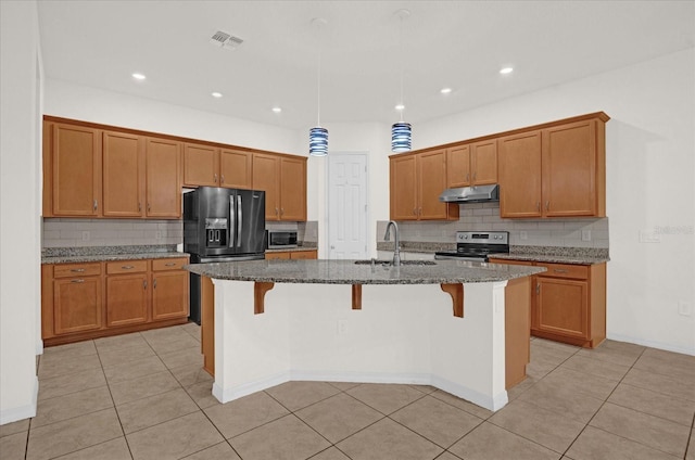 kitchen with appliances with stainless steel finishes, sink, an island with sink, and dark stone counters