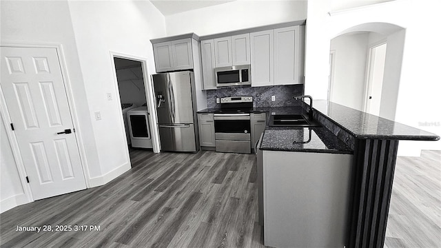 kitchen with sink, appliances with stainless steel finishes, dark stone countertops, tasteful backsplash, and kitchen peninsula