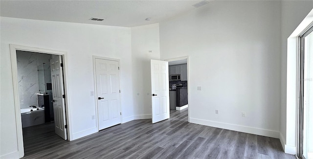 unfurnished bedroom featuring dark hardwood / wood-style floors, high vaulted ceiling, and ensuite bath