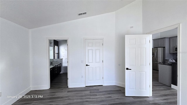 unfurnished bedroom with stainless steel refrigerator with ice dispenser, lofted ceiling, dark wood-type flooring, and ensuite bath