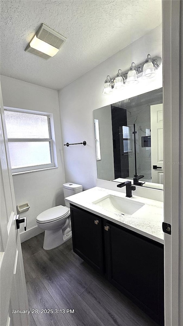 bathroom with toilet, a textured ceiling, a tile shower, vanity, and hardwood / wood-style floors