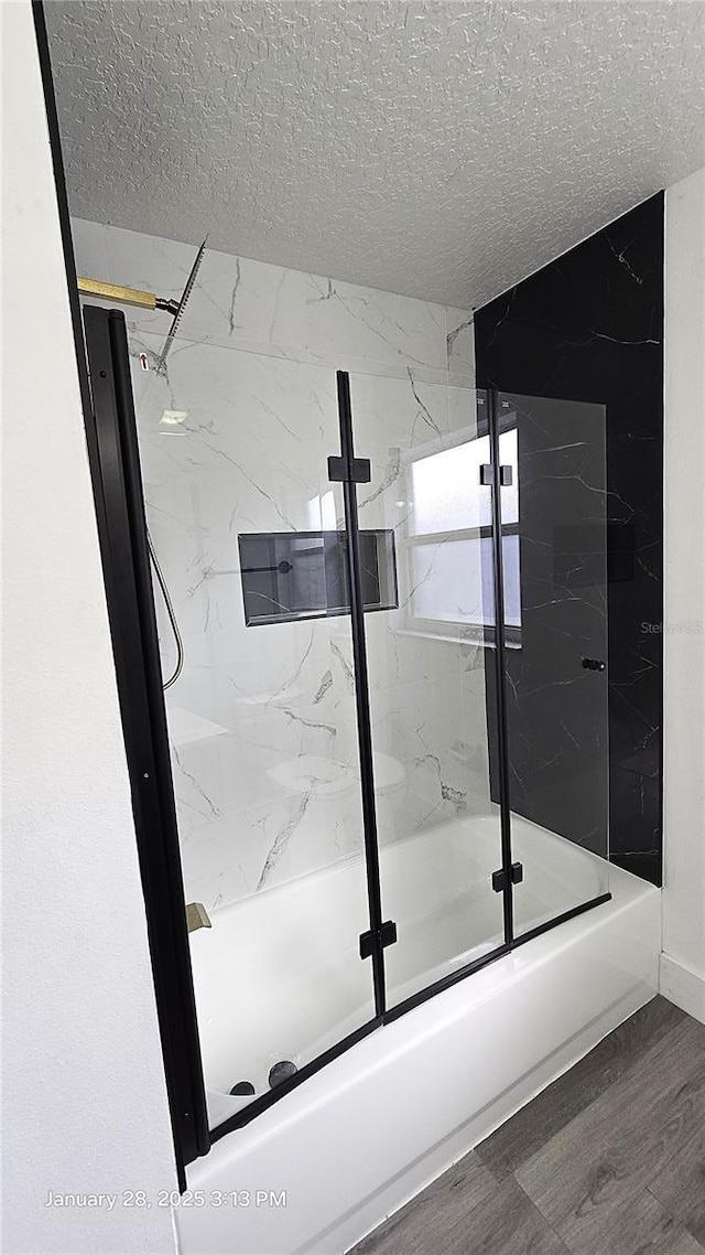 bathroom with hardwood / wood-style flooring, combined bath / shower with glass door, and a textured ceiling