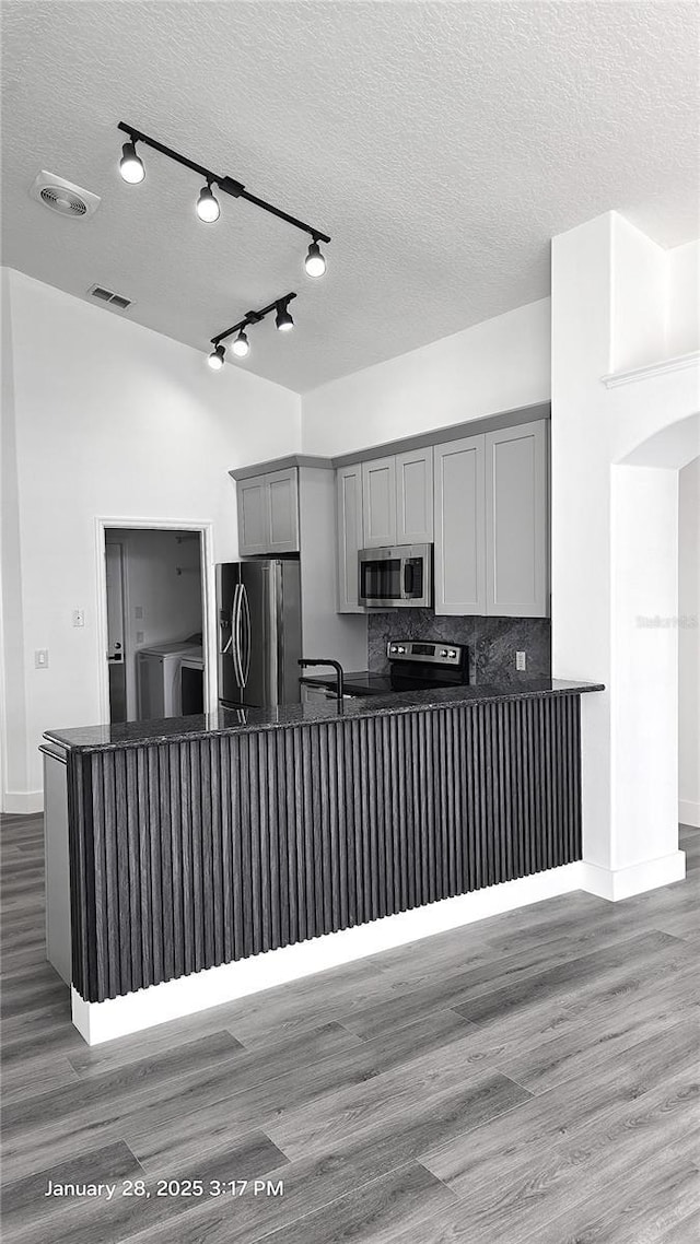 kitchen with appliances with stainless steel finishes, tasteful backsplash, gray cabinetry, light hardwood / wood-style floors, and kitchen peninsula