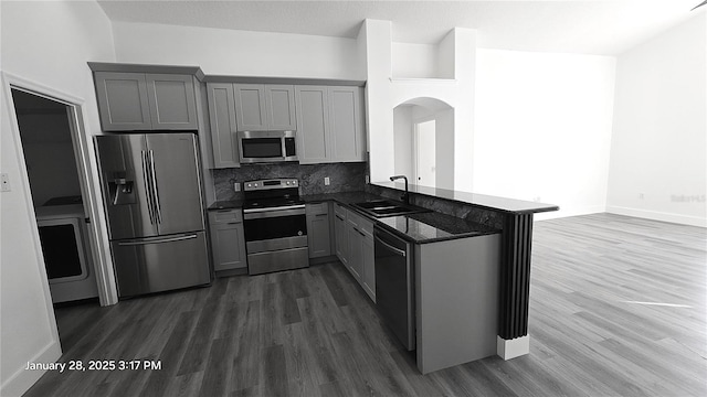 kitchen with sink, appliances with stainless steel finishes, dark hardwood / wood-style flooring, gray cabinets, and kitchen peninsula