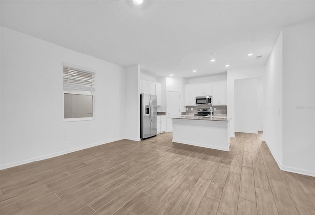 kitchen with white cabinetry, stainless steel appliances, a center island with sink, and light wood-type flooring