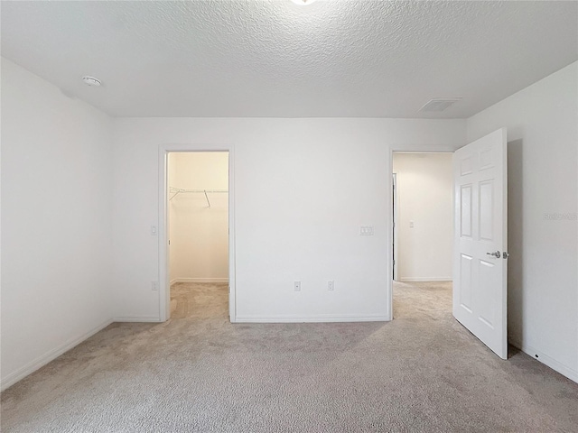 unfurnished bedroom featuring a spacious closet, light colored carpet, and a textured ceiling