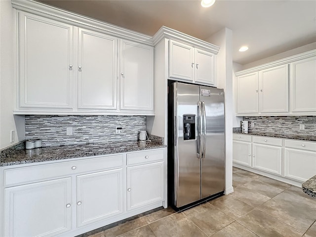 kitchen with light tile patterned floors, stainless steel fridge, white cabinetry, backsplash, and dark stone counters