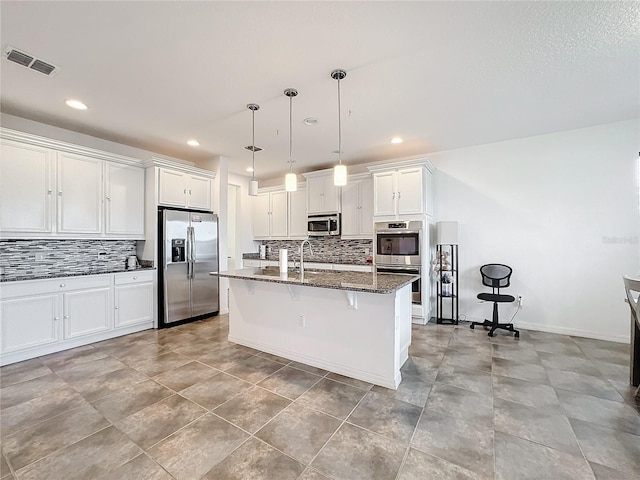 kitchen featuring stainless steel appliances, white cabinetry, an island with sink, and dark stone counters