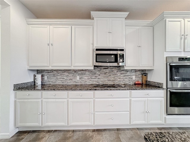 kitchen featuring white cabinetry, stainless steel appliances, tasteful backsplash, and dark stone countertops