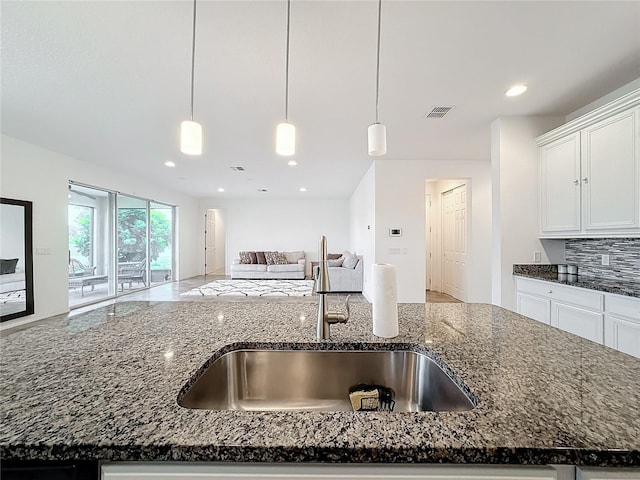 kitchen with sink, a kitchen island with sink, hanging light fixtures, and dark stone countertops