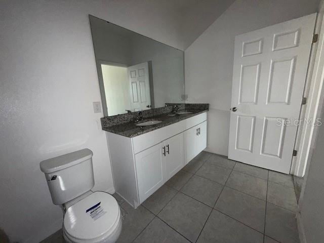 bathroom with tile patterned floors, lofted ceiling, toilet, and vanity