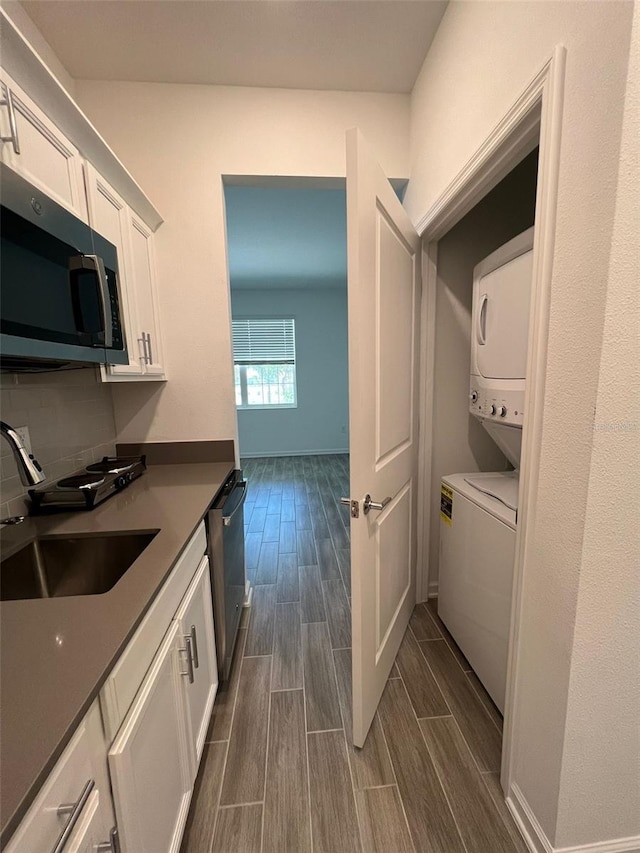 interior space with white cabinetry, sink, stainless steel appliances, and stacked washing maching and dryer