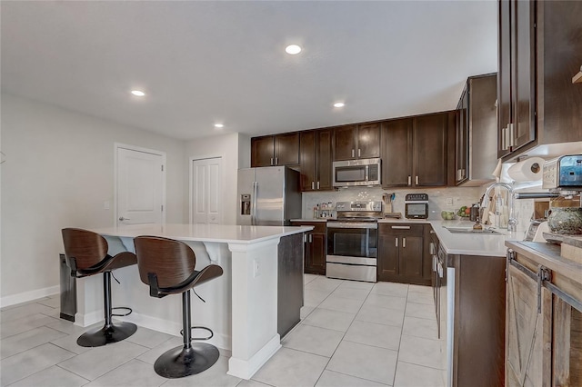 kitchen with sink, a center island, light tile patterned floors, appliances with stainless steel finishes, and a kitchen breakfast bar