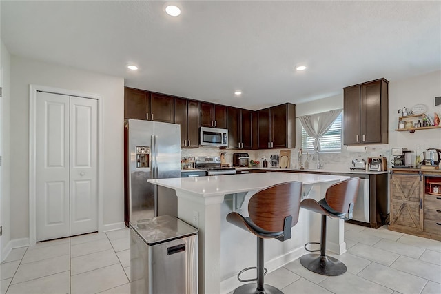 kitchen featuring light tile patterned floors, appliances with stainless steel finishes, backsplash, a kitchen breakfast bar, and a kitchen island