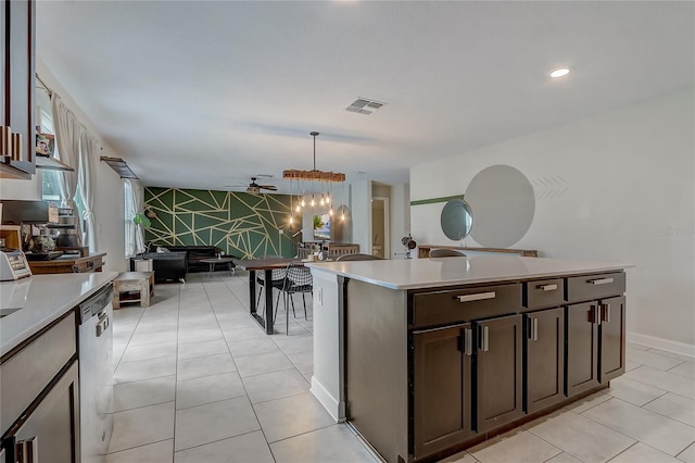 kitchen featuring dark brown cabinets, hanging light fixtures, light tile patterned floors, dishwasher, and a kitchen island with sink